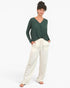 A woman modeling a dark green long-sleeve V-neck top paired with cream-colored wide-leg pants, standing against a plain white studio background.