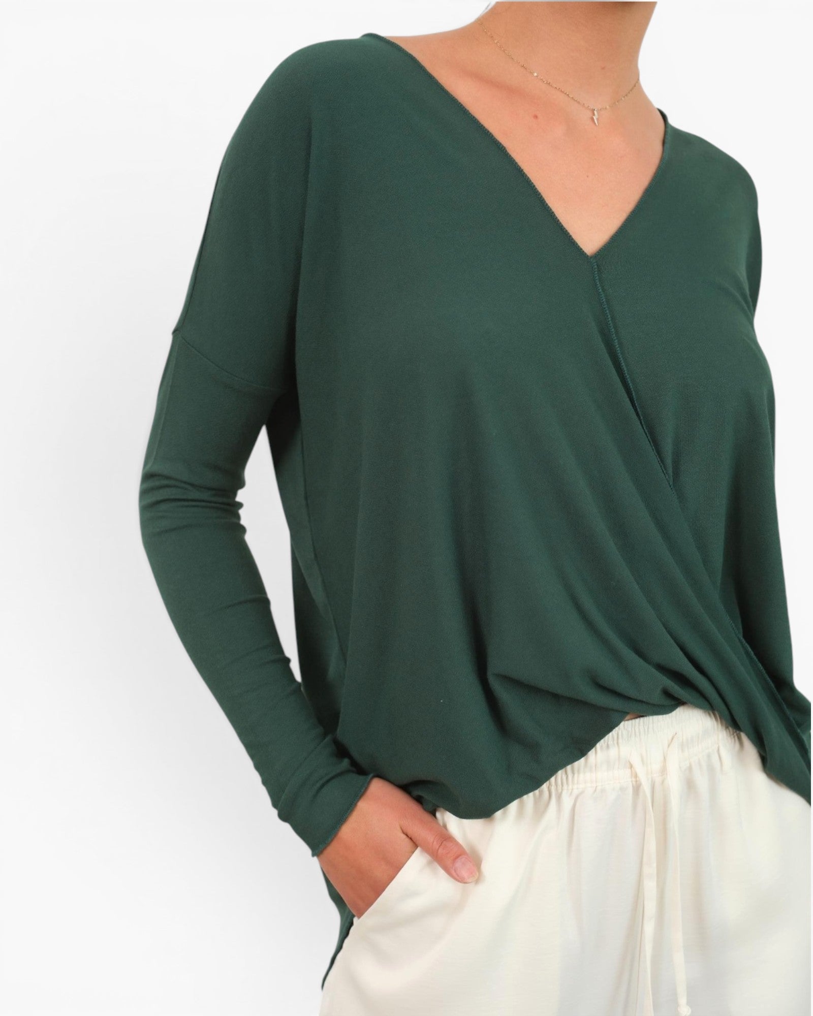 A woman wearing a dark green long-sleeve wrap-style top with a V-neck, paired with white drawstring pants, shown against a plain white background.