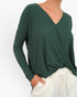 A woman wearing a dark green long-sleeve wrap-style top with a V-neck, paired with white drawstring pants, shown against a plain white background.
