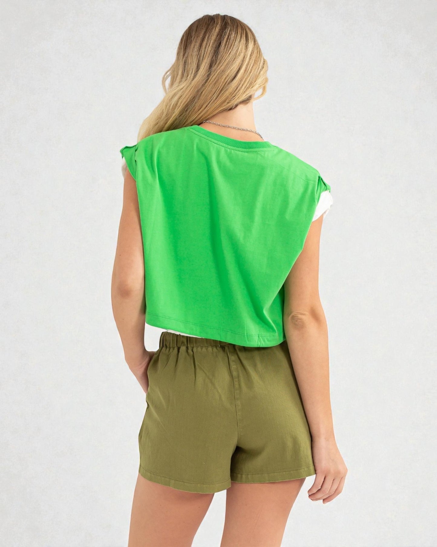 Person wearing a green sleeveless top and olive shorts on a white background