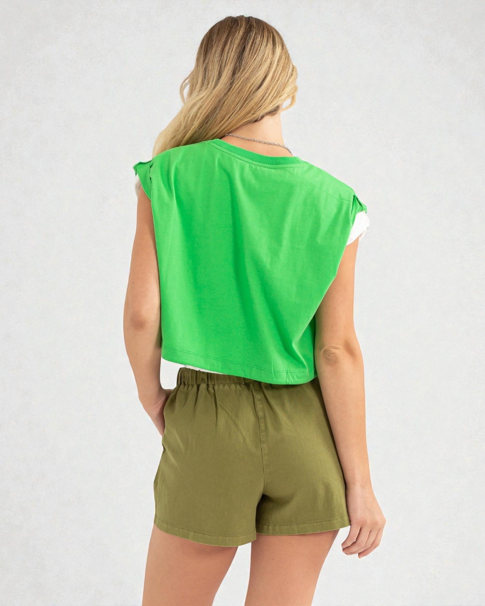 Person wearing a green sleeveless top and olive shorts on a white background