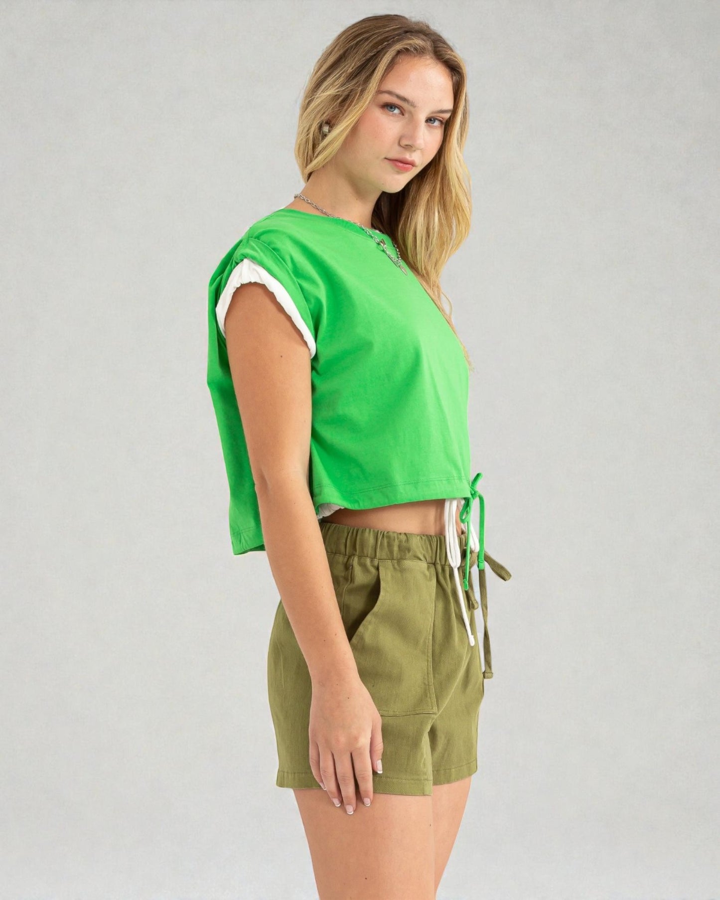 Woman wearing a green crop top and olive green shorts on a gray background