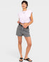 A woman modeling a light pink cropped tie-front t-shirt and gray patterned shorts with a black belt, paired with black slide sandals, against a light gray studio background.