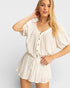 Woman wearing a beige romper against a plain background