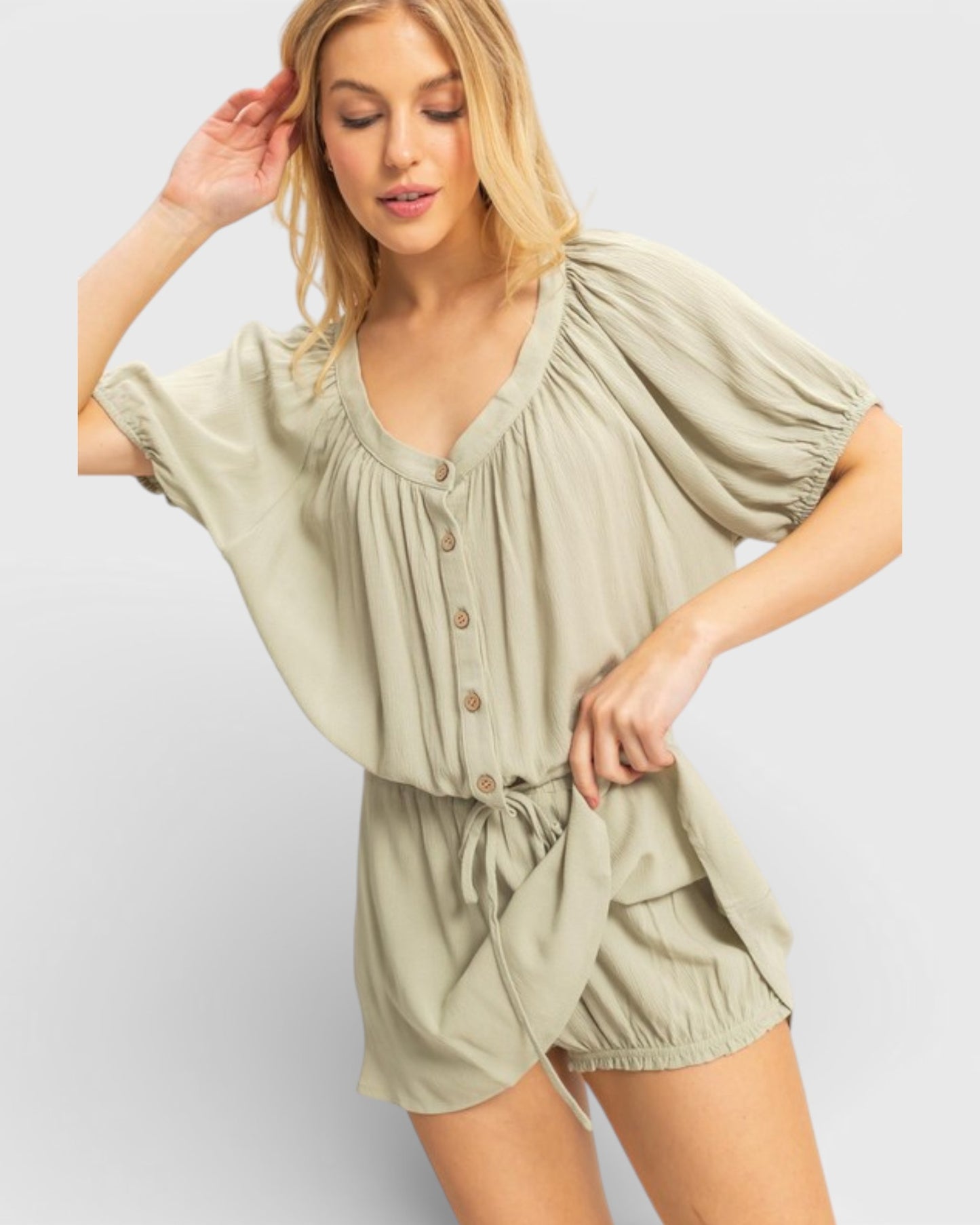 Woman wearing a light green romper on a plain background