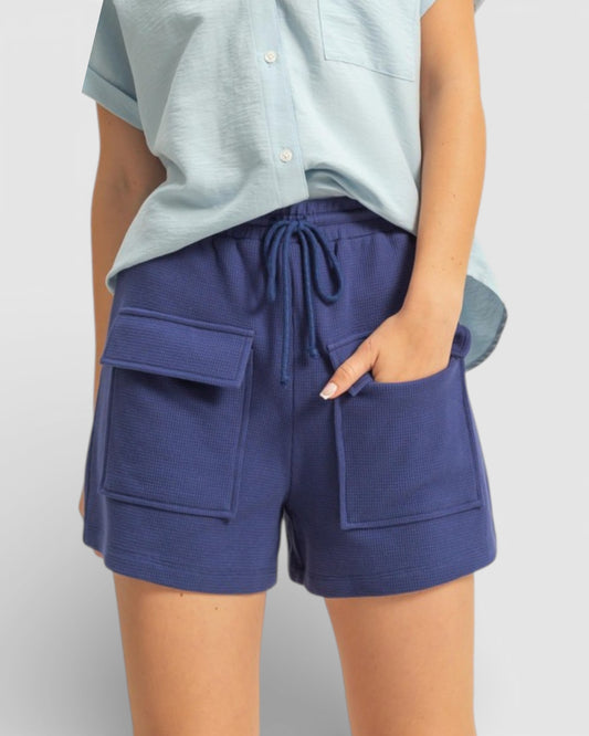 Person wearing blue shorts with pockets on a plain background