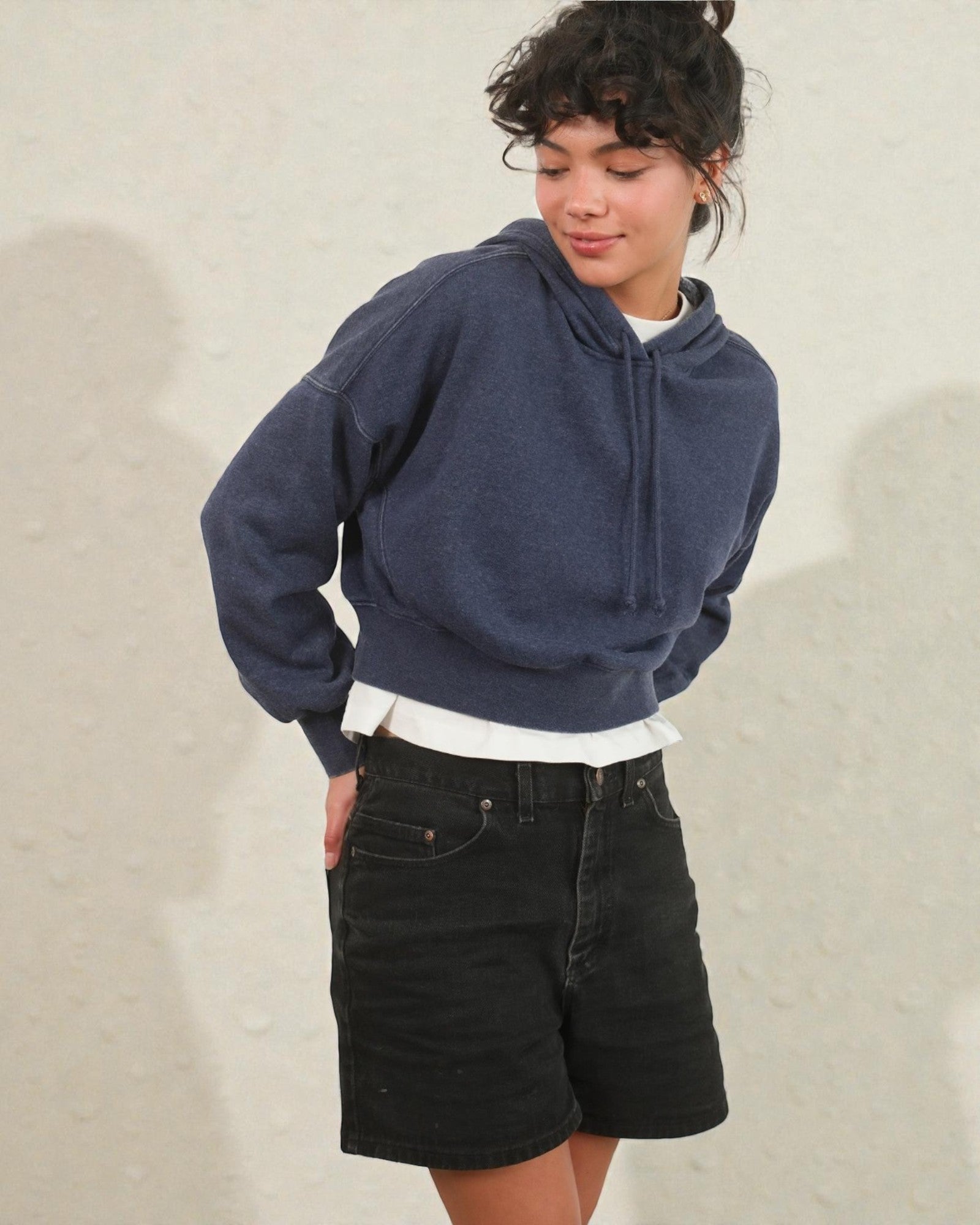 Person wearing a blue hoodie and black shorts on a neutral background