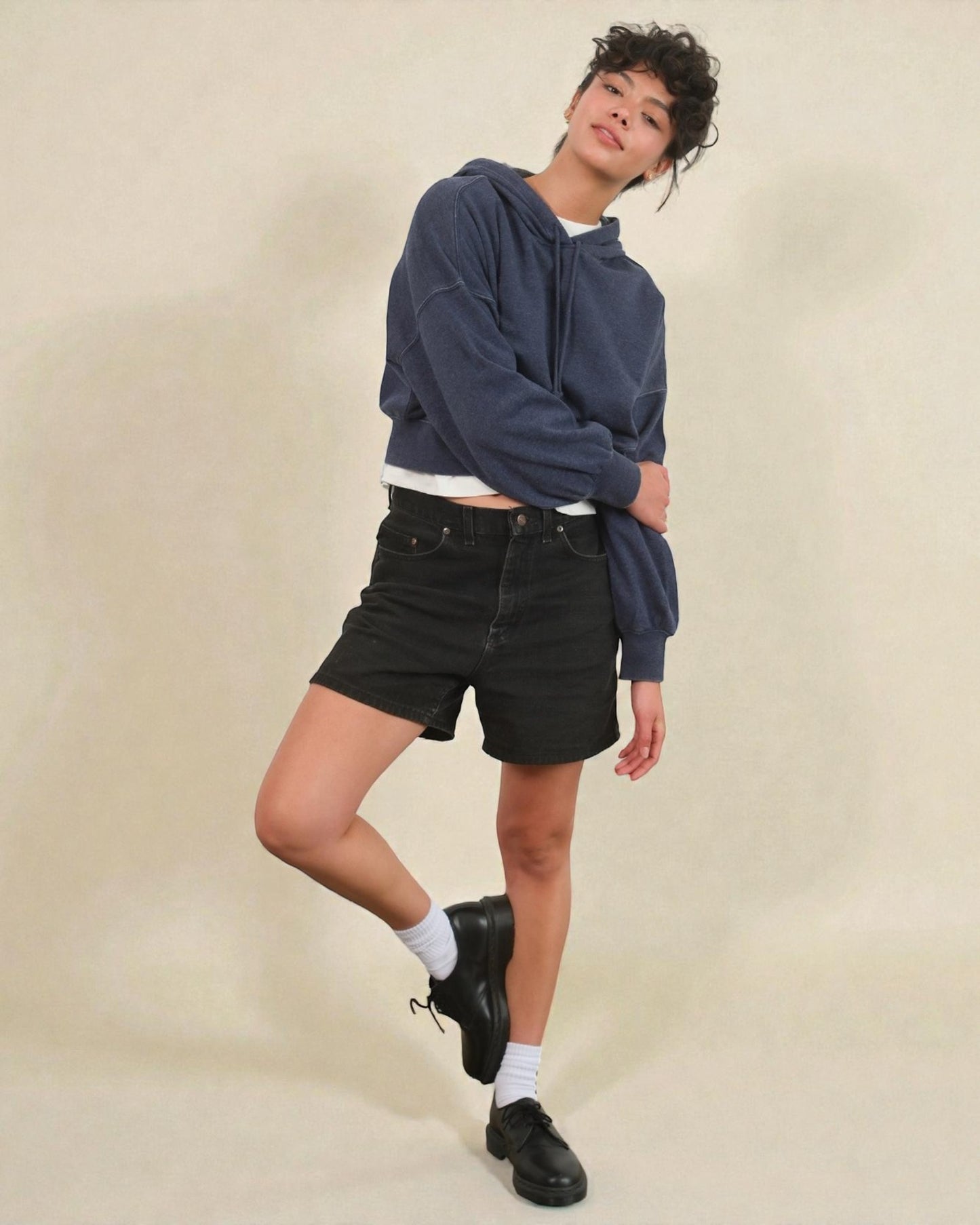 Person wearing a navy hoodie and black shorts on a beige background