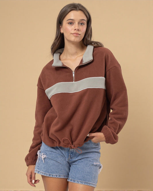Woman wearing a brown and gray pullover with denim shorts on a beige background