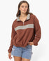 A woman modeling a rust-brown half-zip sweatshirt with a contrasting light gray collar and horizontal chest stripe, paired with light-wash denim shorts against a plain white background.