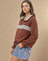 Woman wearing a brown and gray pullover with denim shorts against a beige background