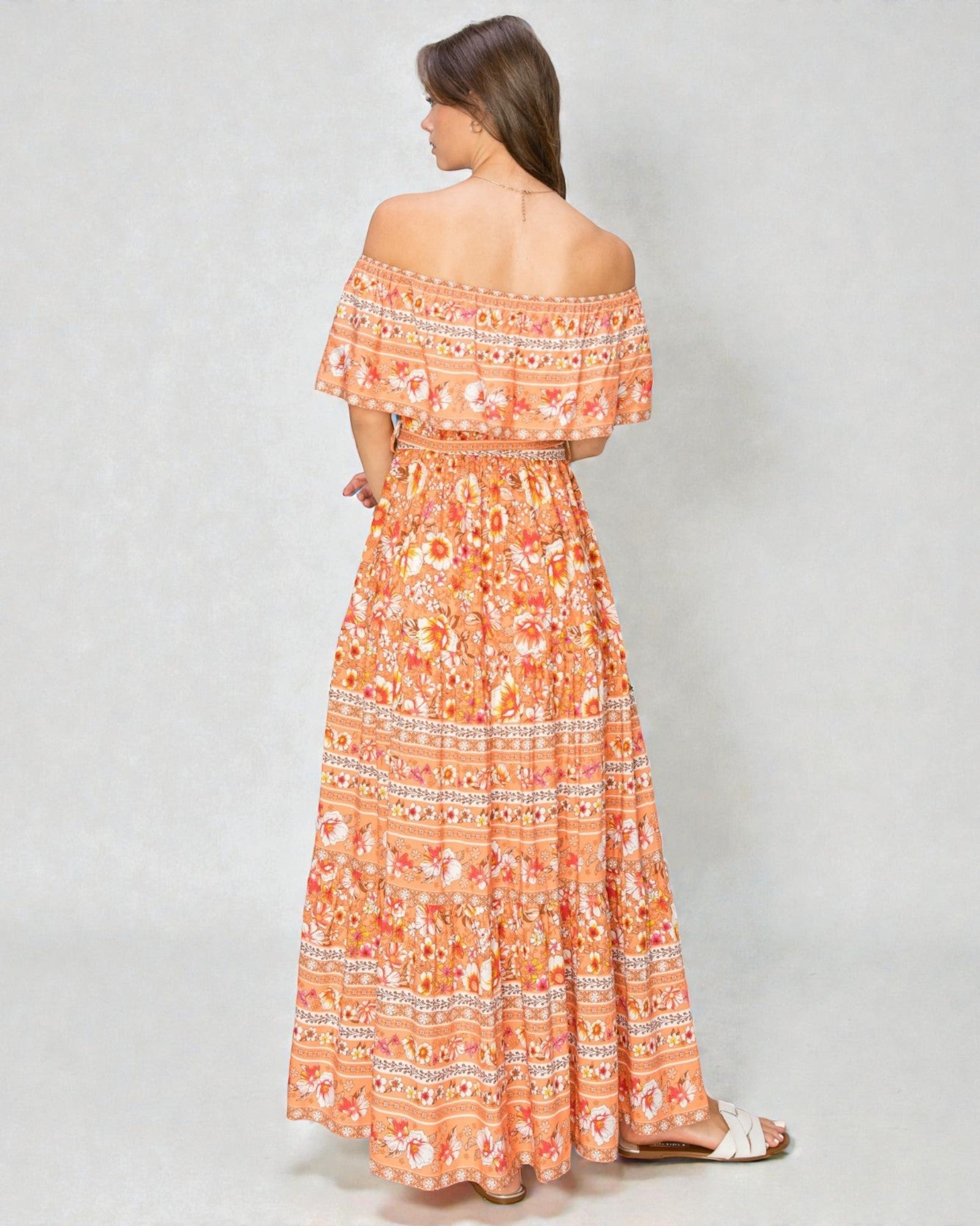 Woman wearing an orange floral off-shoulder dress on a gray background