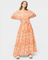 A woman modeling an off-the-shoulder maxi dress with a vibrant orange, peach, and white bohemian-style floral pattern, set against a solid light gray background.