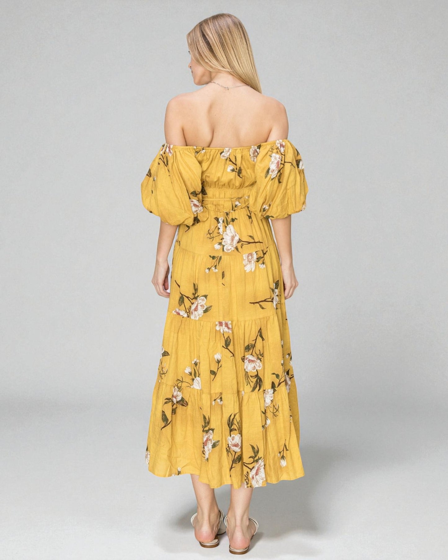 Woman wearing a yellow floral off-shoulder dress on a gray background