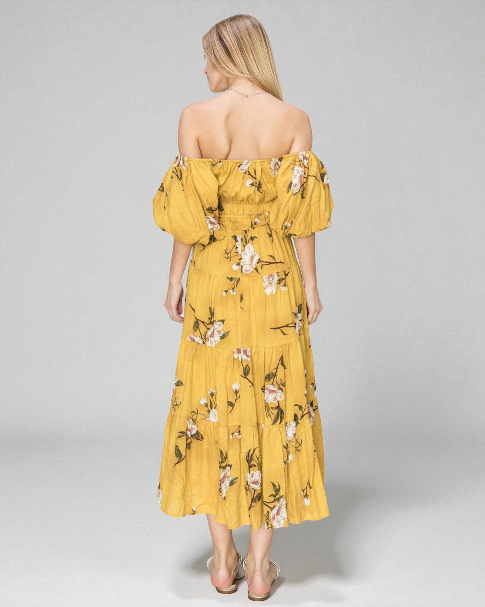 Woman wearing a yellow floral off-shoulder dress on a gray background
