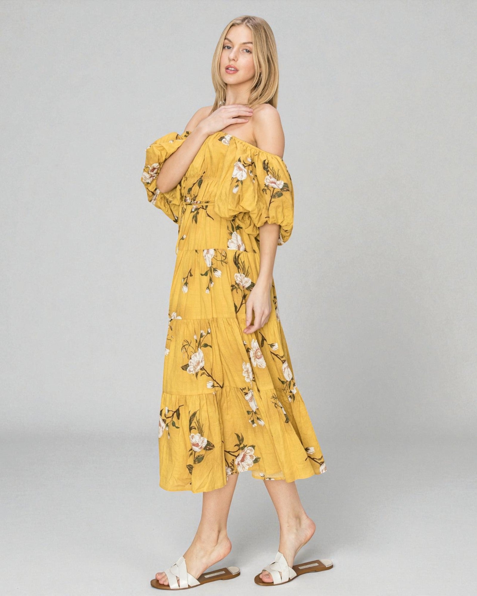 Woman wearing a yellow floral off-shoulder dress on a gray background