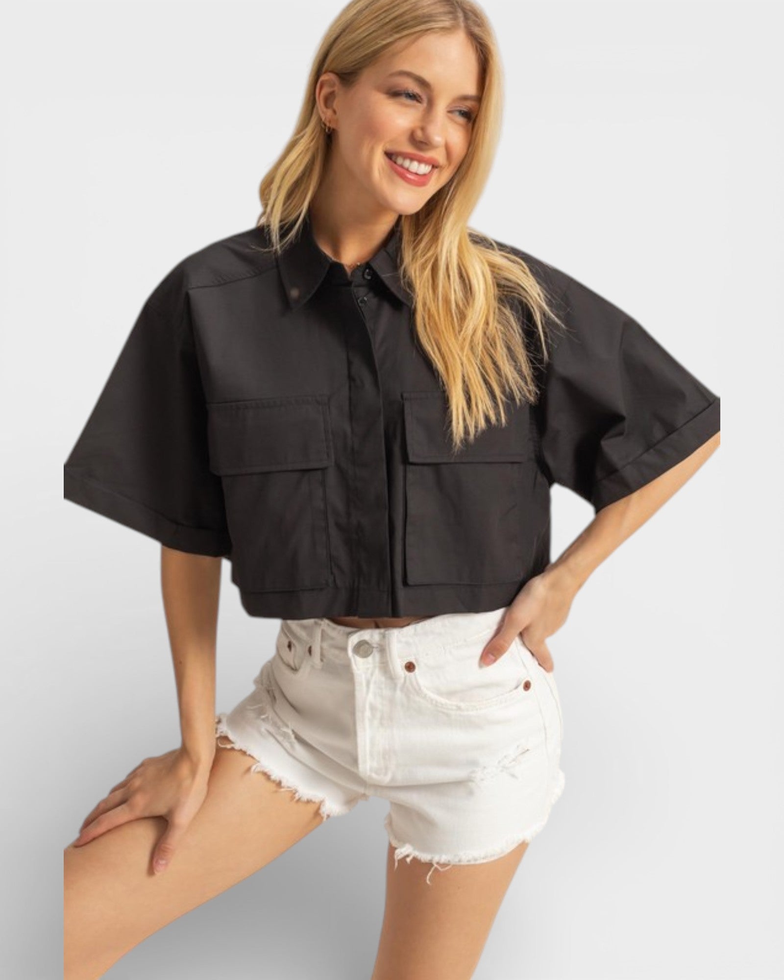 Woman wearing a black cropped jacket and white shorts on a light gray background