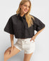Woman wearing a black cropped jacket and white shorts on a light gray background