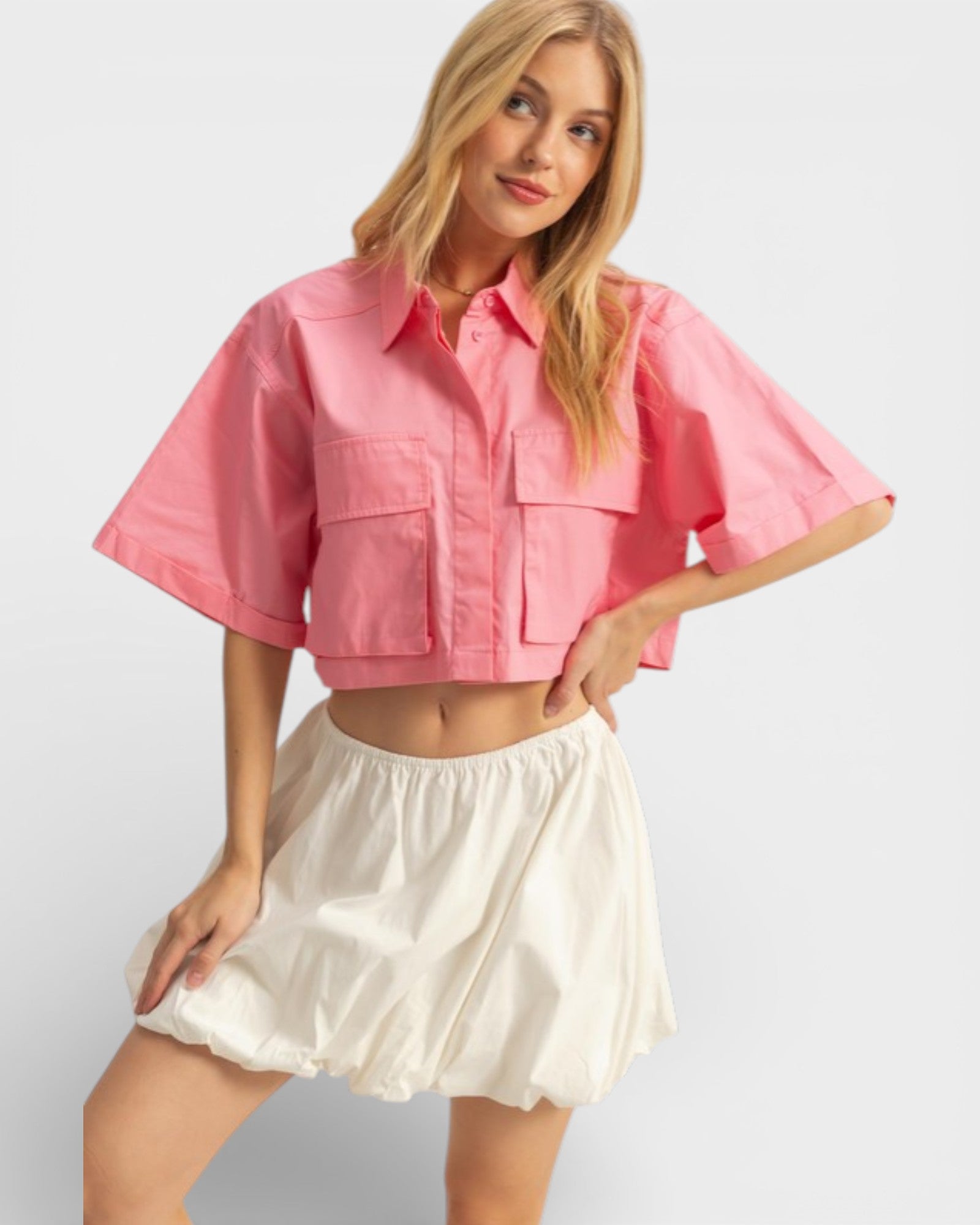 Woman wearing a pink cropped jacket and white skirt on a light gray background