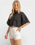 Woman wearing a black cropped jacket and white shorts on a light gray background