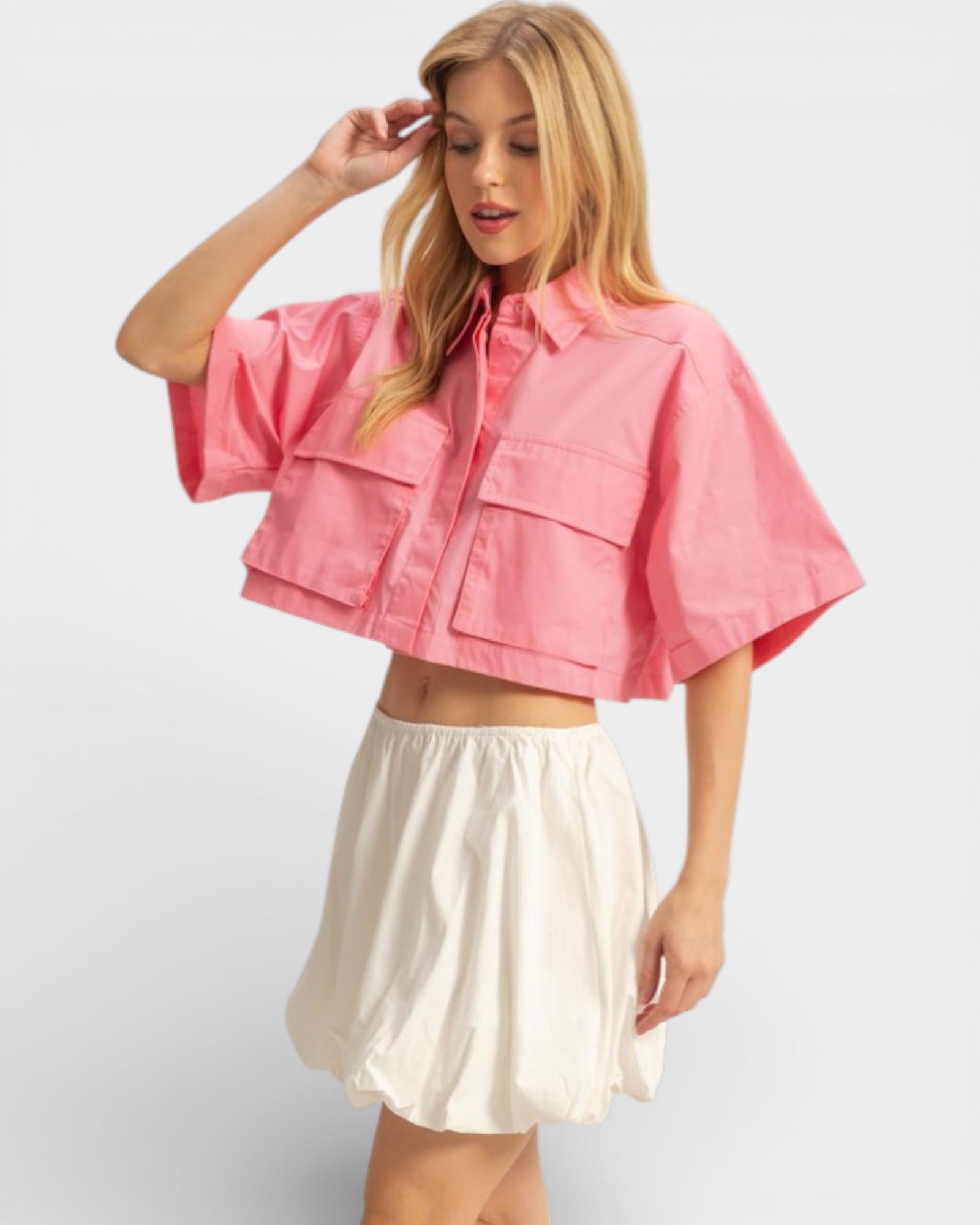 Woman wearing a pink cropped top and white skirt on a light gray background
