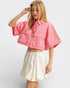Woman wearing a pink cropped top and white skirt on a light gray background
