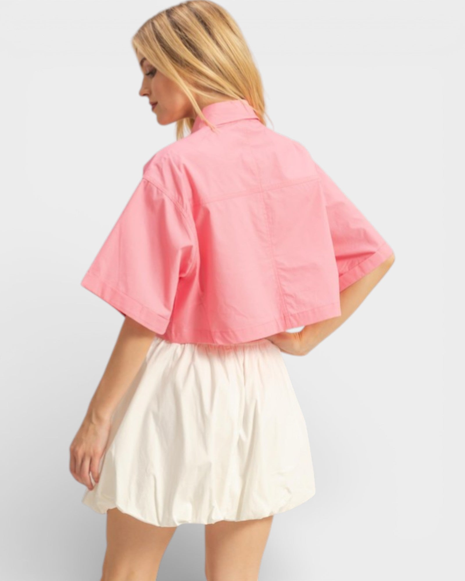 Woman wearing a pink shirt and white skirt on a plain background
