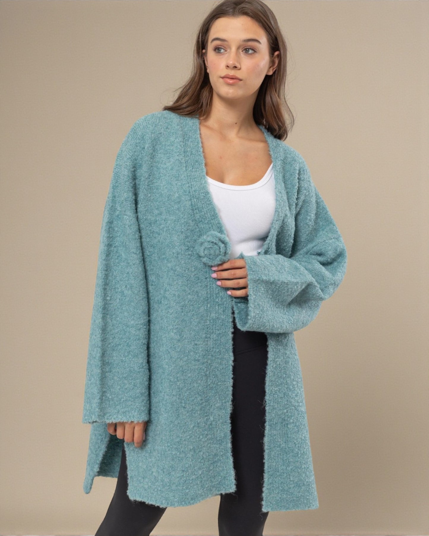 Woman wearing a teal cardigan over a white top and black pants on a beige background