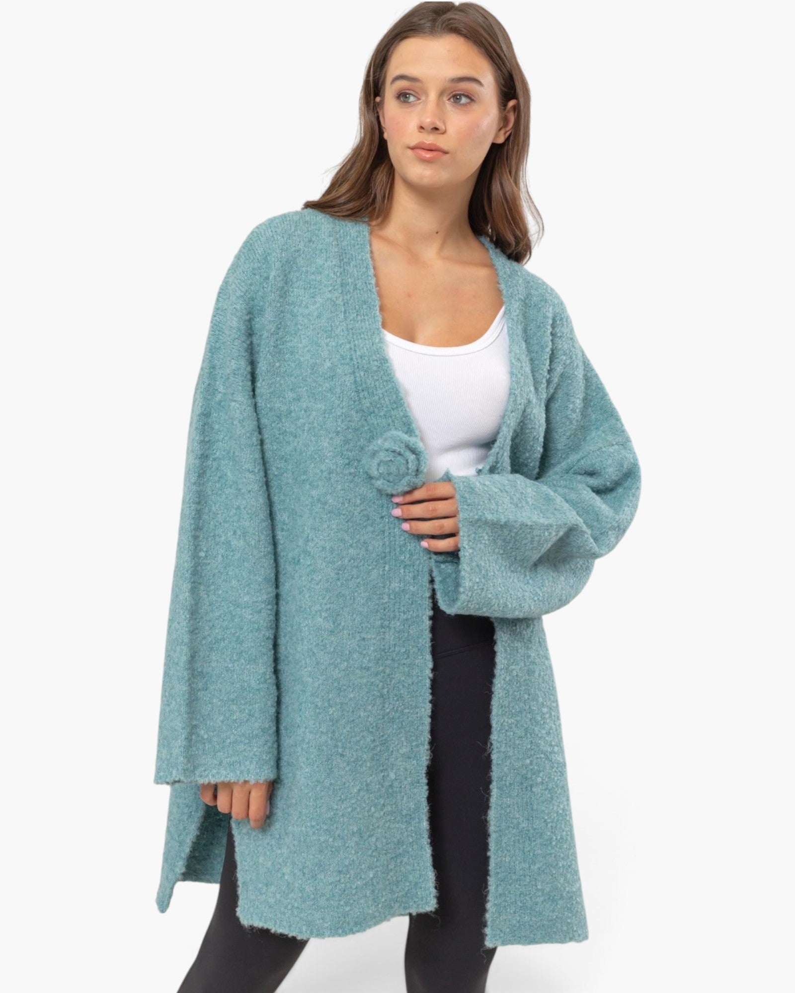 A woman modeling a fuzzy, open-front cardigan in a dusty teal blue color, worn over a white tank top and black pants against a plain white background.