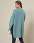 Woman wearing a teal poncho against a beige background
