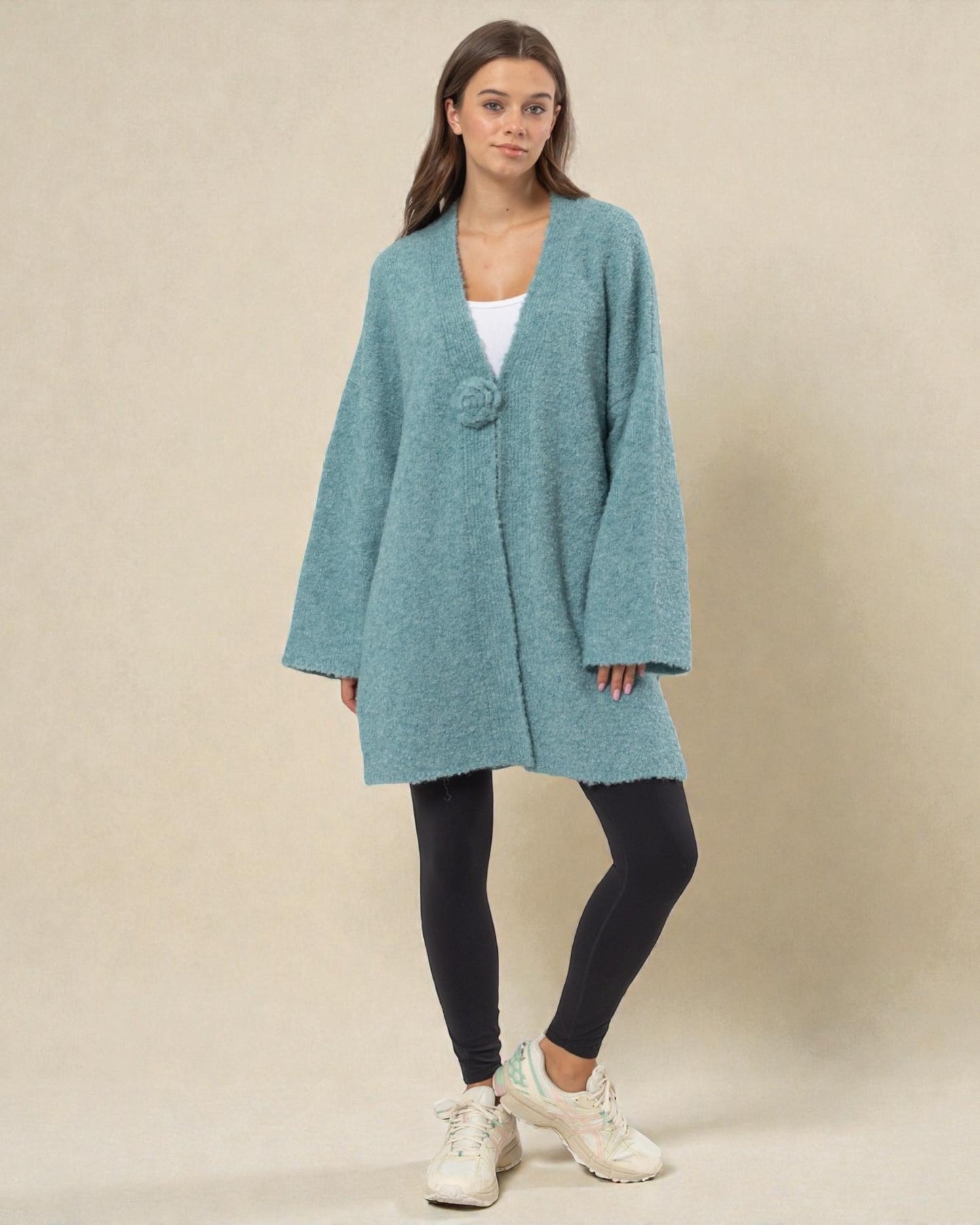 Woman wearing a teal cardigan over a white top on a beige background