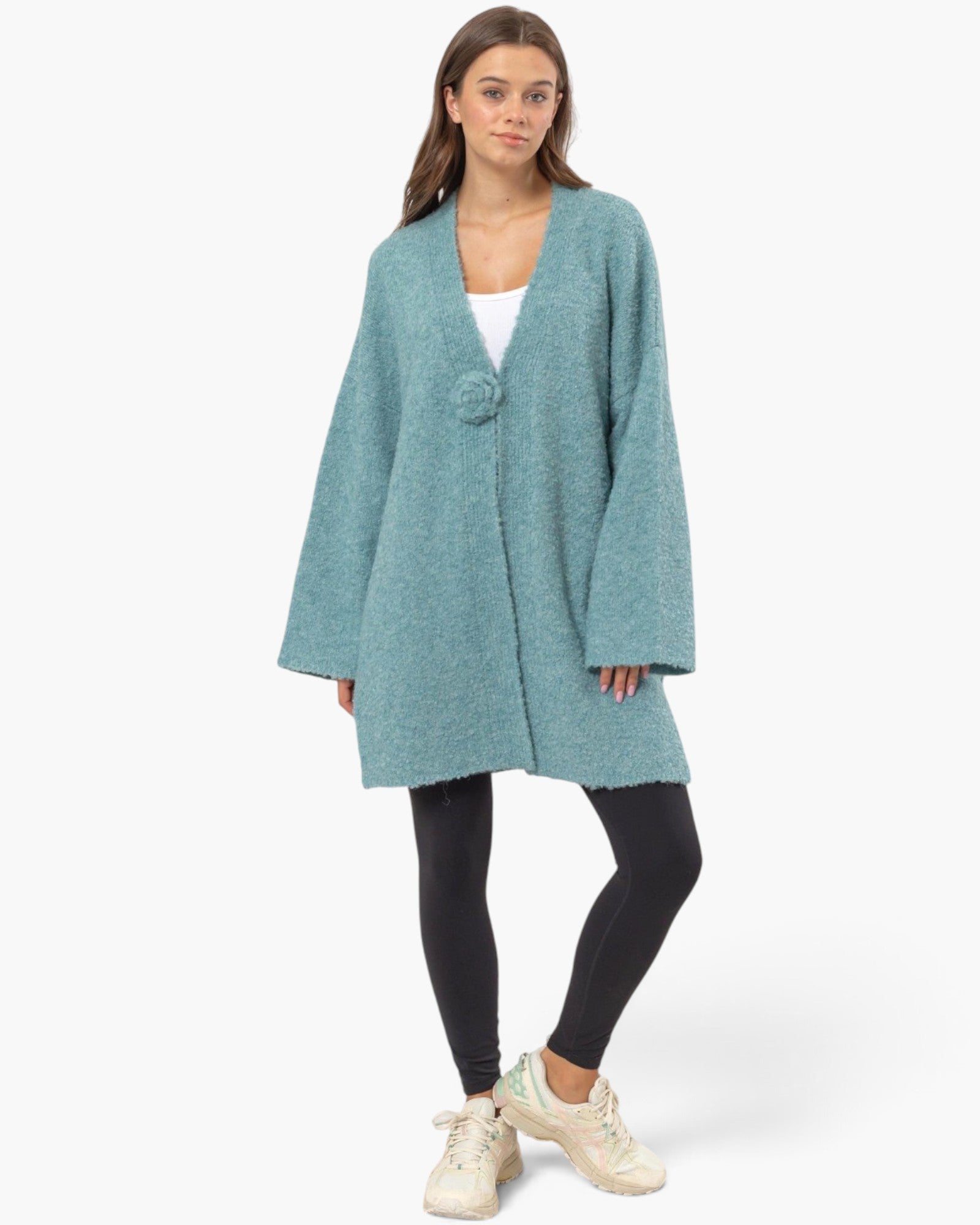 A woman modeling a heathered teal blue open-front cardigan with long sleeves, styled over a white top, black leggings, and cream sneakers against a light gray studio background.