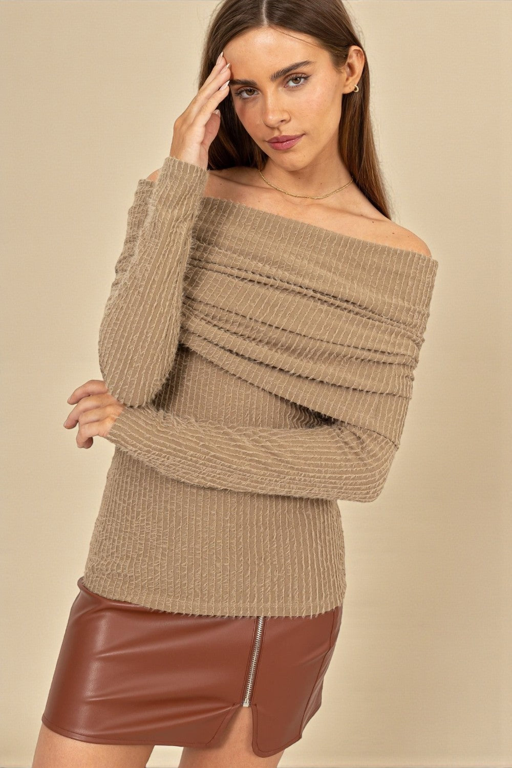 Woman wearing a beige off-shoulder sweater and brown leather skirt against a beige background