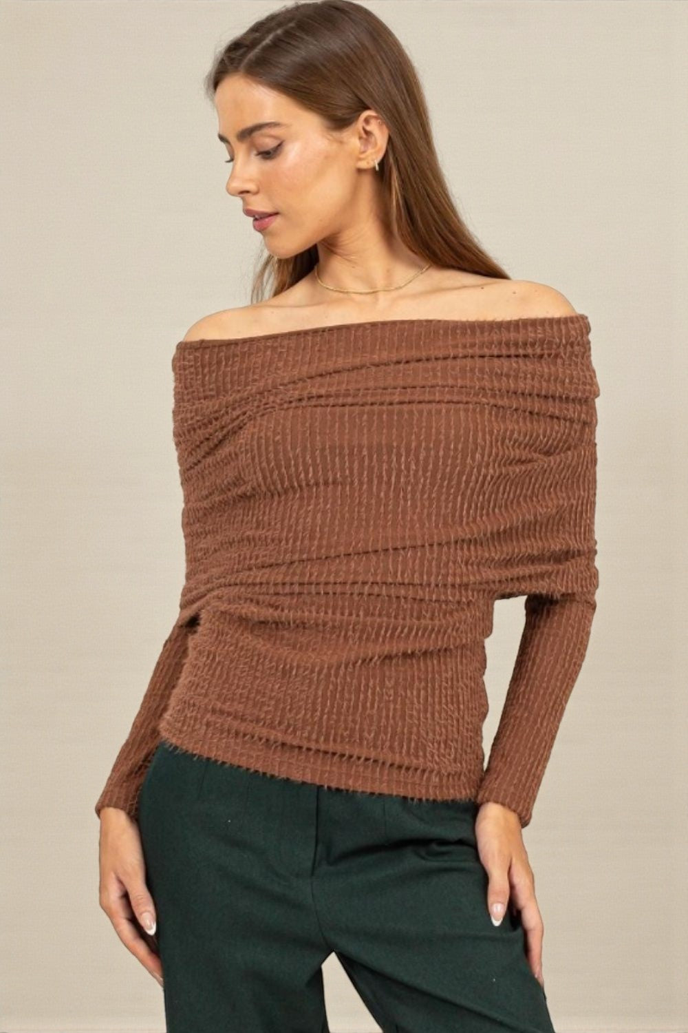 Woman wearing a brown off-shoulder sweater against a beige background