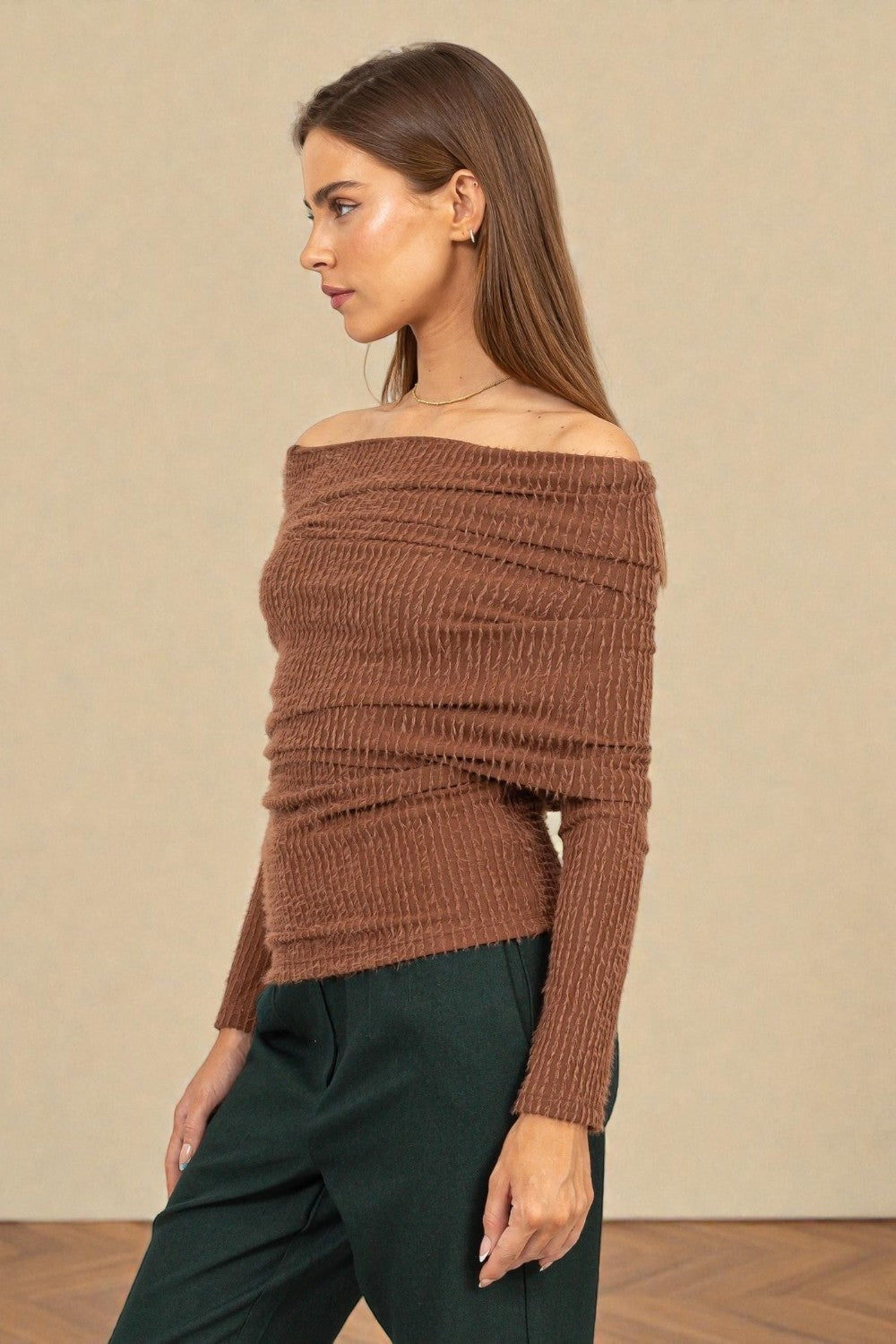 Woman wearing a brown off-shoulder sweater against a beige background