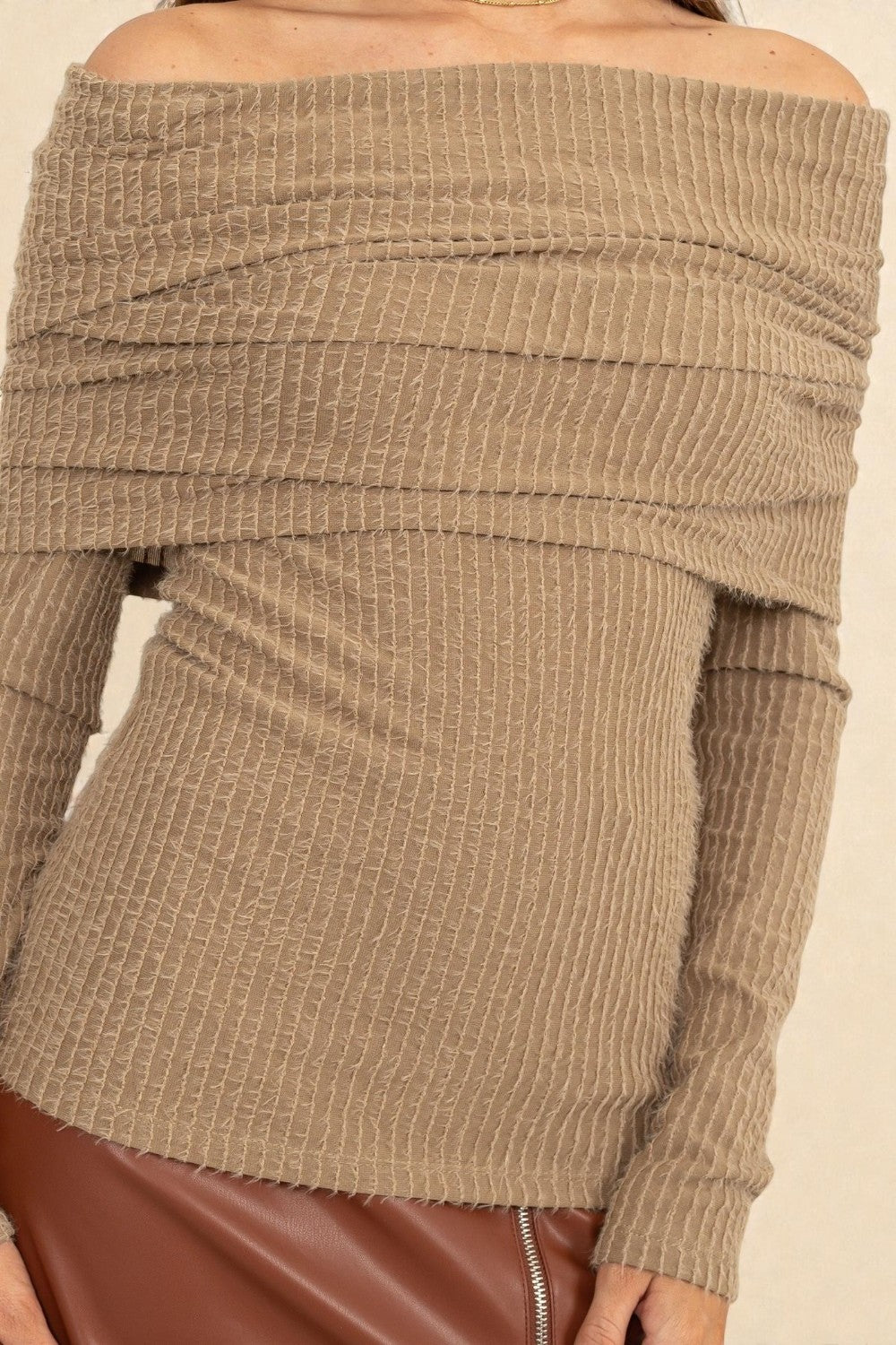 Close-up of a beige ribbed sweater with off-shoulder design.
