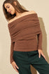 Woman wearing a brown off-shoulder sweater and green pants against a beige background