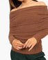 A close-up of a woman wearing a brown off-the-shoulder ribbed knit sweater, showing her hands adjusting the hem, against a plain white background.