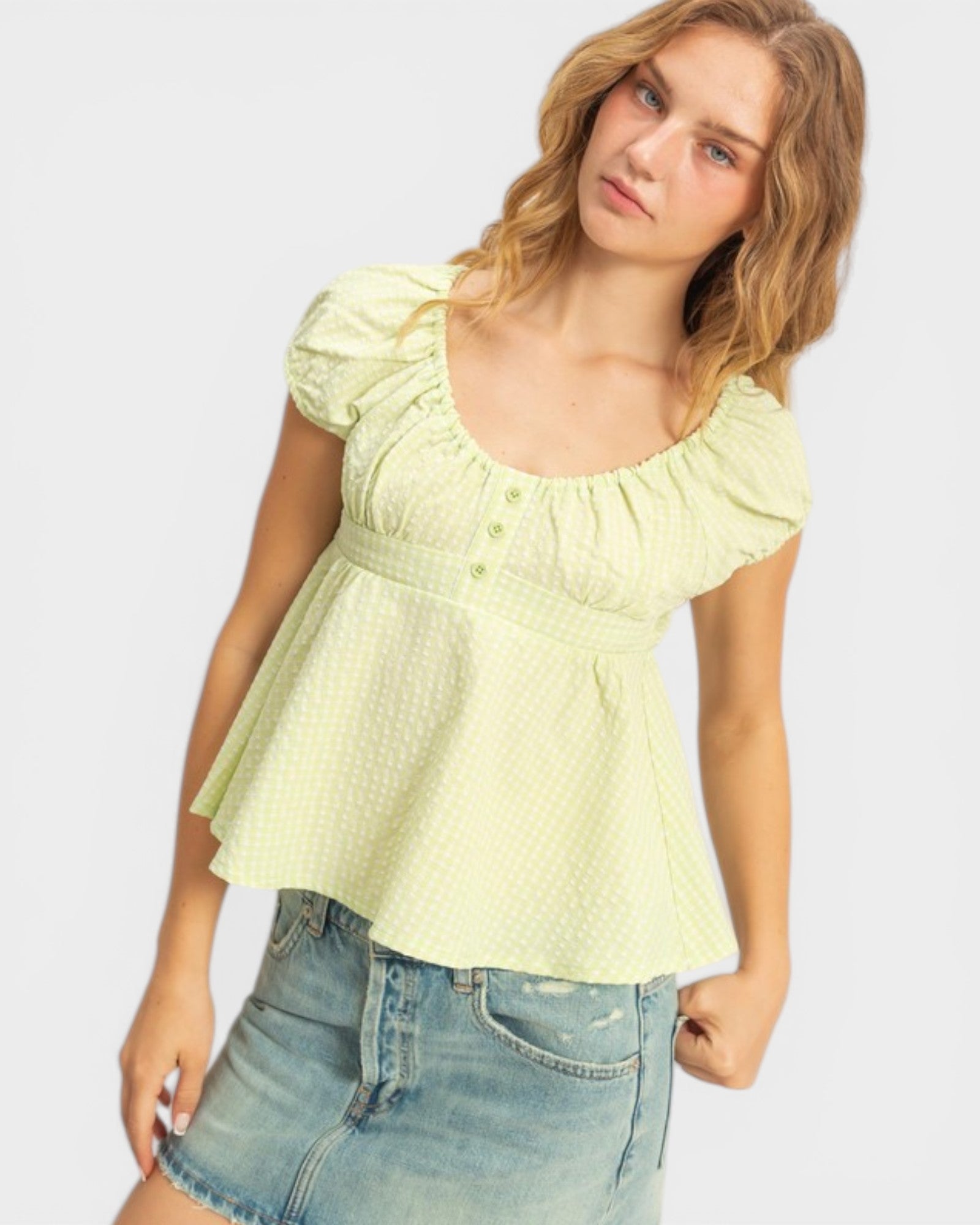 Woman wearing a light green blouse and denim shorts on a plain background