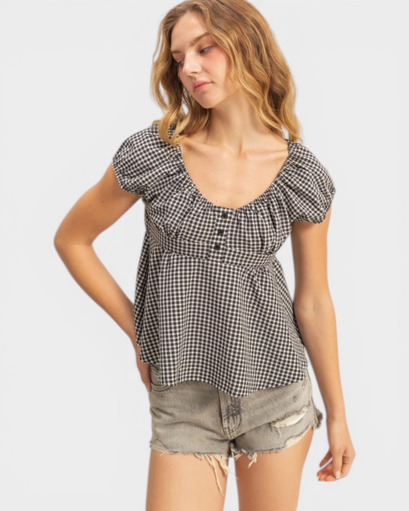 Woman wearing a black and white checkered top with denim shorts on a white background
