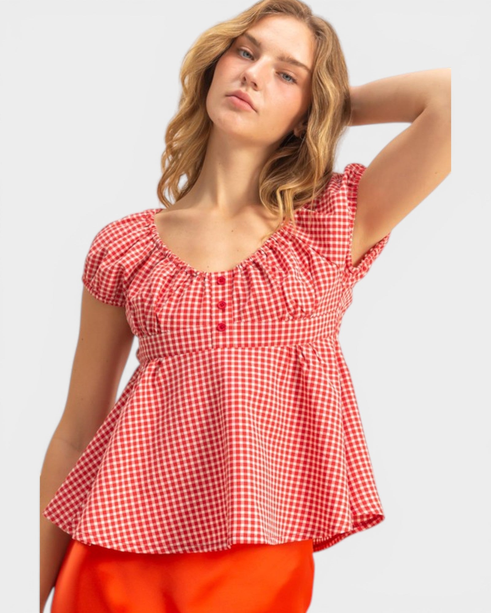 Woman wearing a red and white checkered top with orange pants on a light gray background