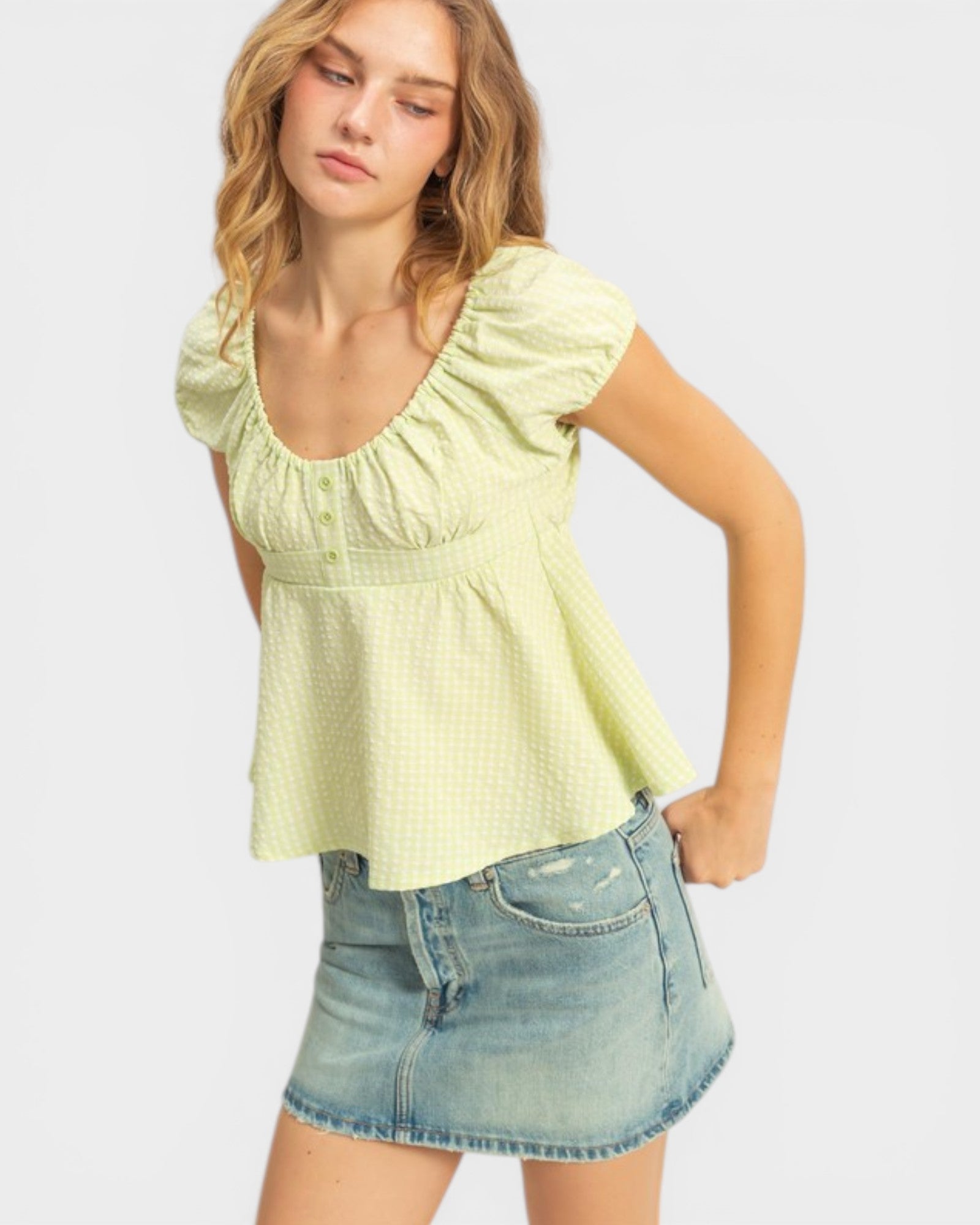 Woman wearing a light green top and denim skirt on a white background