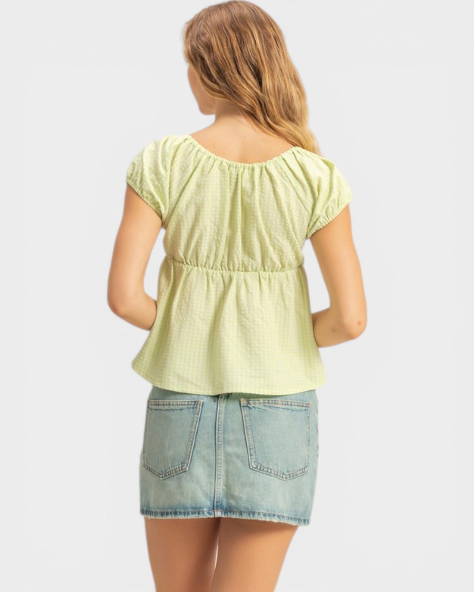 Woman wearing a light green top and denim skirt on a white background