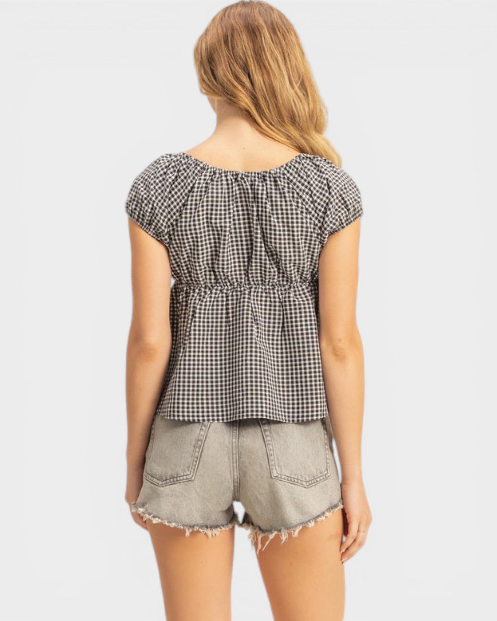 Woman wearing a black and white checkered top and light denim shorts on a white background