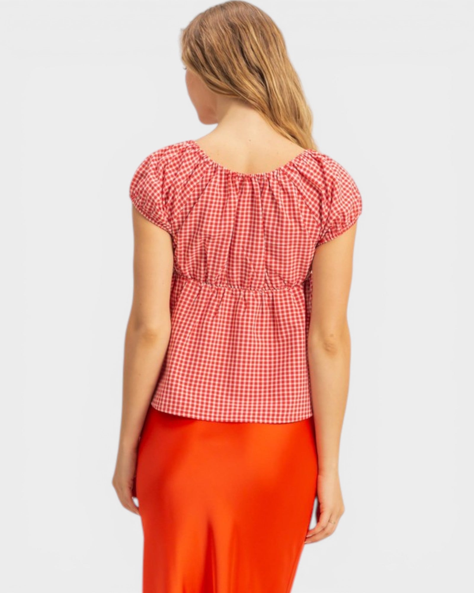 Woman wearing a red and white checkered top with red pants on a light gray background