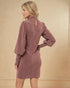 Woman wearing a pink dress with long sleeves against a beige background