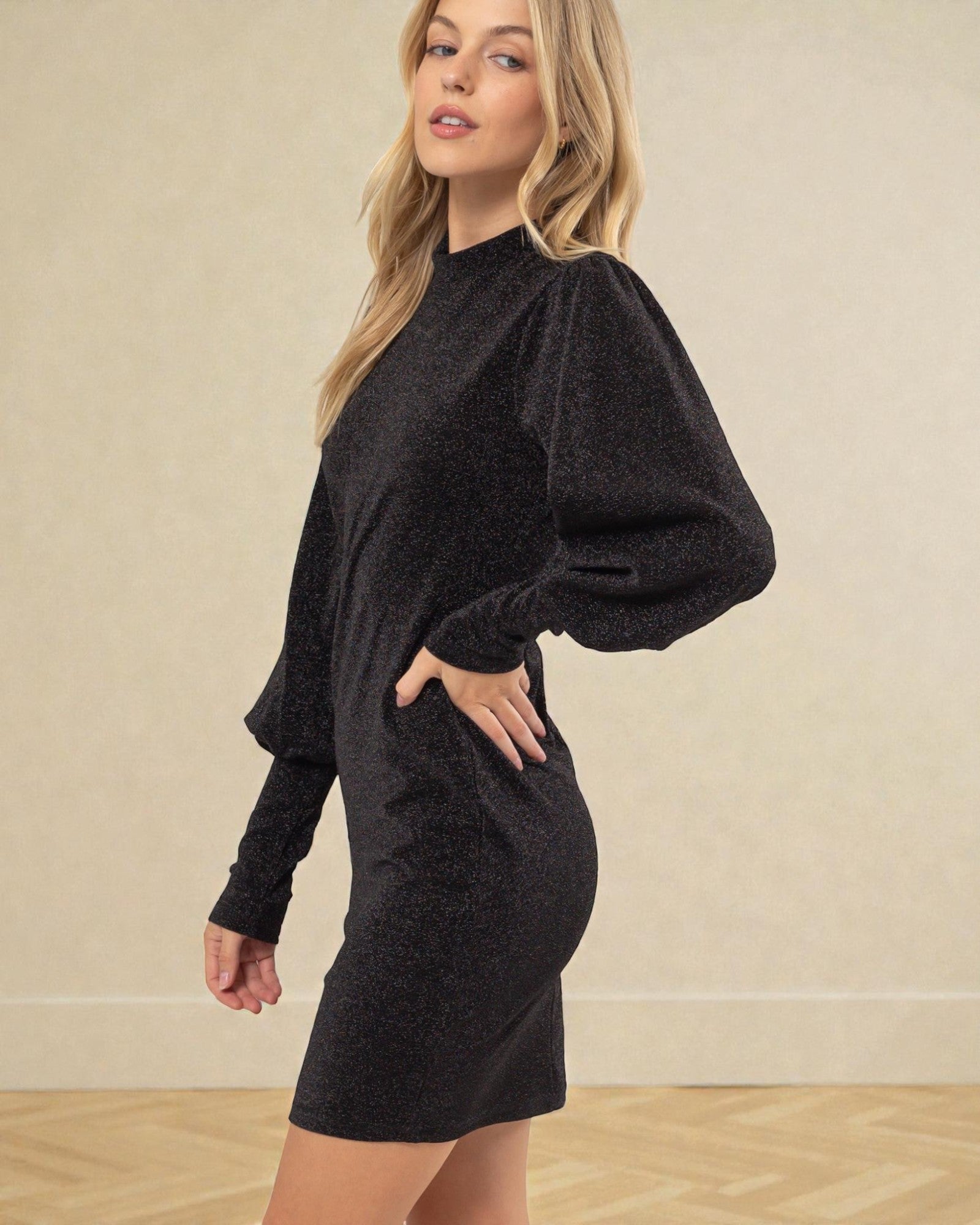 Woman wearing a black dress with puffed sleeves against a beige background