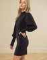 Woman wearing a black dress with puffed sleeves against a beige background