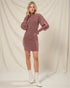 Woman wearing a mauve dress with puffed sleeves against a plain background