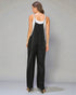 Woman wearing a black overalls with a white top against a gray background